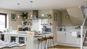 A modern kitchen with white cabinetry, a central island with stools, pendant lighting, and a view of the outdoors through a window. - Heron's Nest -  Ripple, Gloucester, Tewkesbury, sleeping two guests (Ripple)