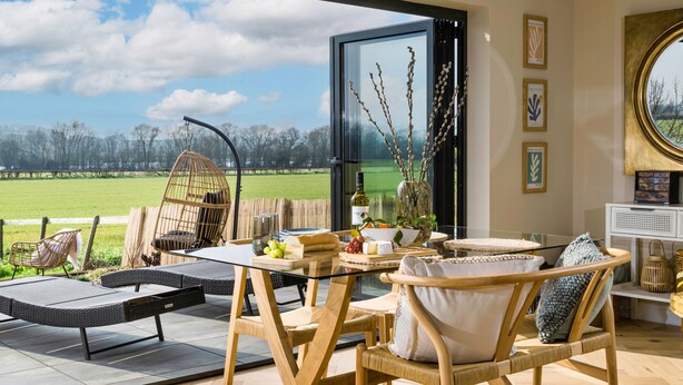 A dining area with wicker furniture, a glass table, and a view of a green field. - Heron's Nest -  Ripple, Gloucester, Tewkesbury, sleeping two guests (Ripple)