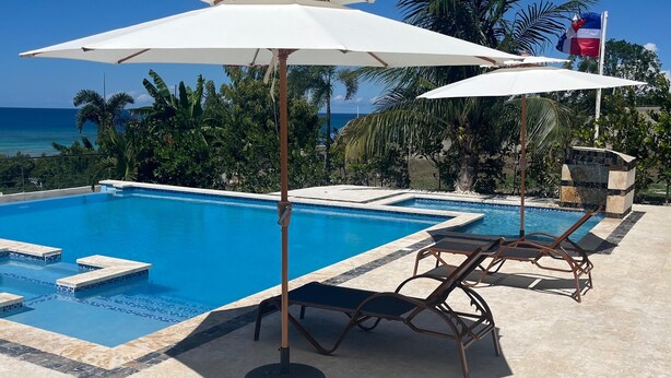 A swimming pool with lounge chairs and umbrellas, surrounded by palm trees and a view of the ocean. - Luxury BeachFront Villa with Private pool and Ocean View!
 (Punta Rucia)