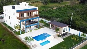 A modern two-story house with a large swimming pool, a covered patio, and a well-maintained lawn. - Luxury BeachFront Villa with Private pool and Ocean View!
 (Punta Rucia)