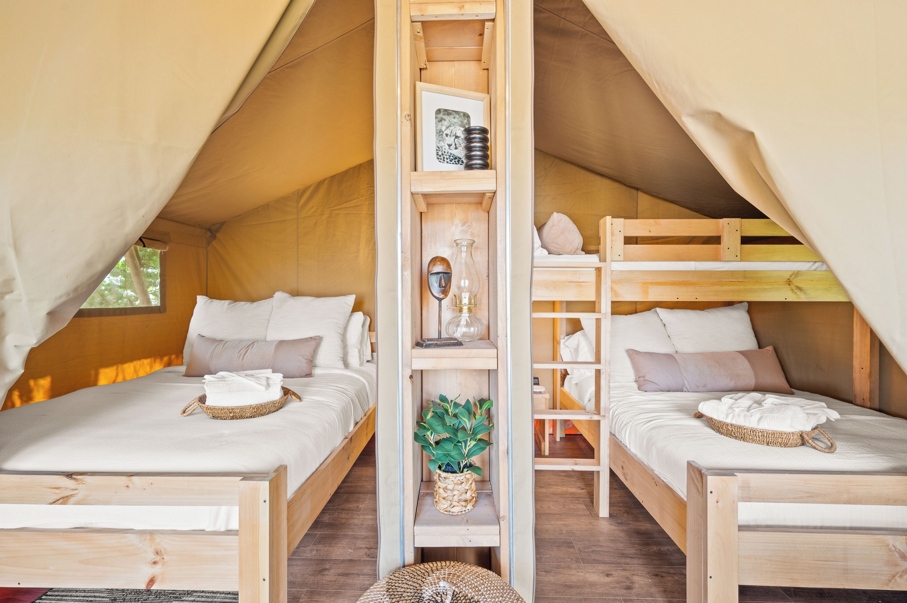 A cozy tent with two wooden beds, a central shelf with a plant, and a small table.