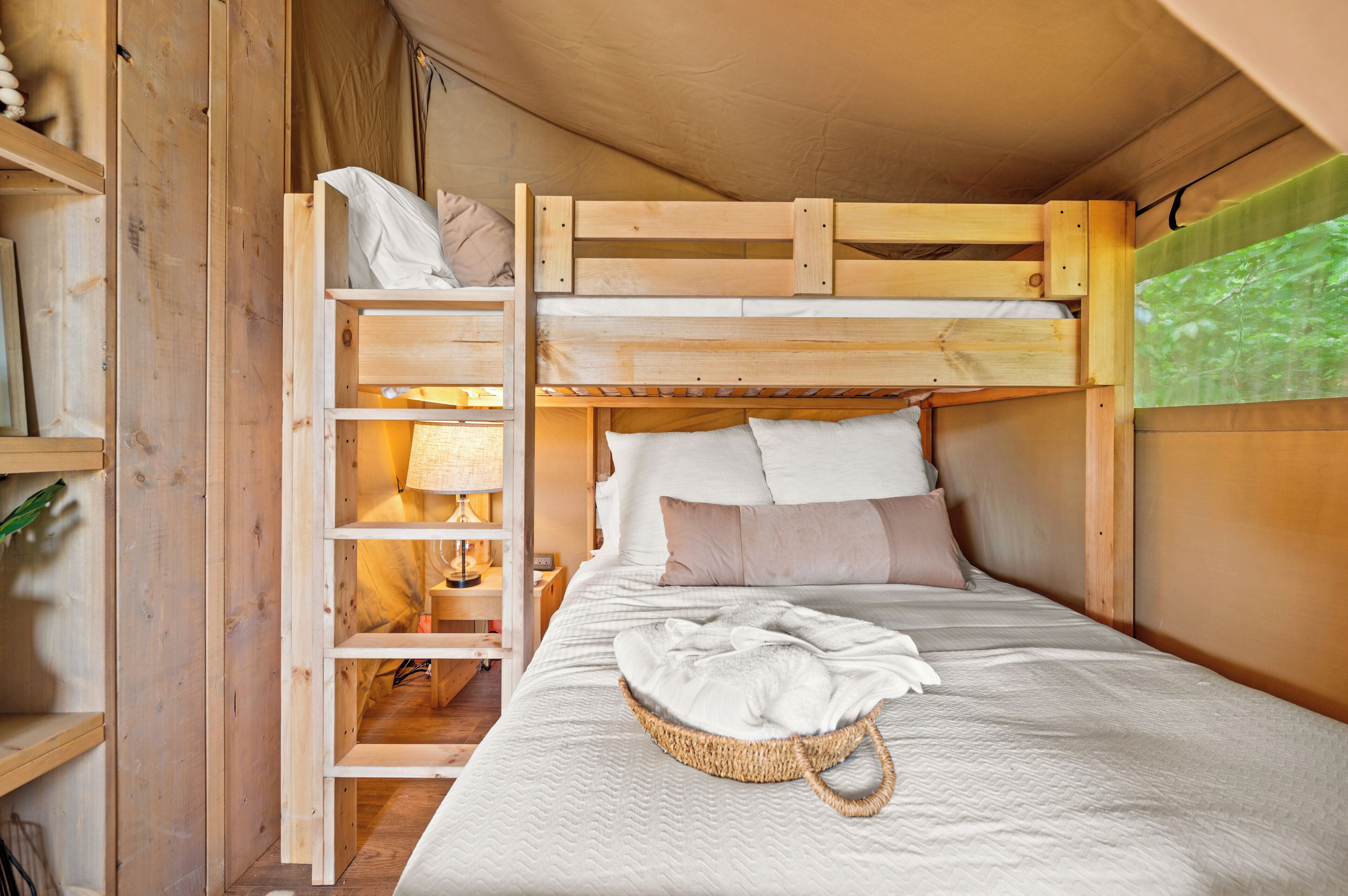A bunk bed with a ladder, a bedside table with a lamp, and a basket on the bed.