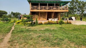 Una casa de madera de dos pisos con un balcón, rodeada de vegetación y un cielo despejado.