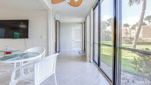 Een balkon met een eettafel en stoelen, een plafondventilator en een aan de muur bevestigde televisie.