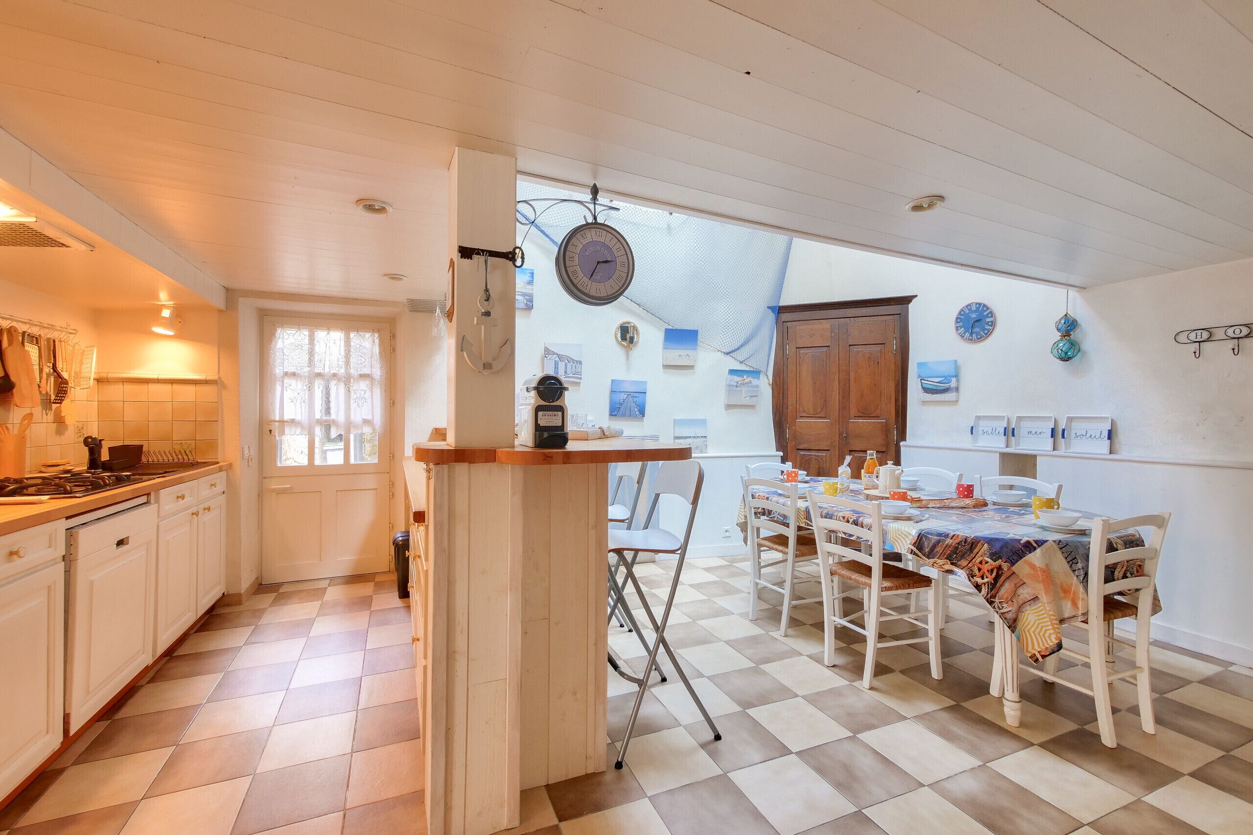 A kitchen with a wooden island, white cabinets, and a dining area with a checkered floor and white chairs.