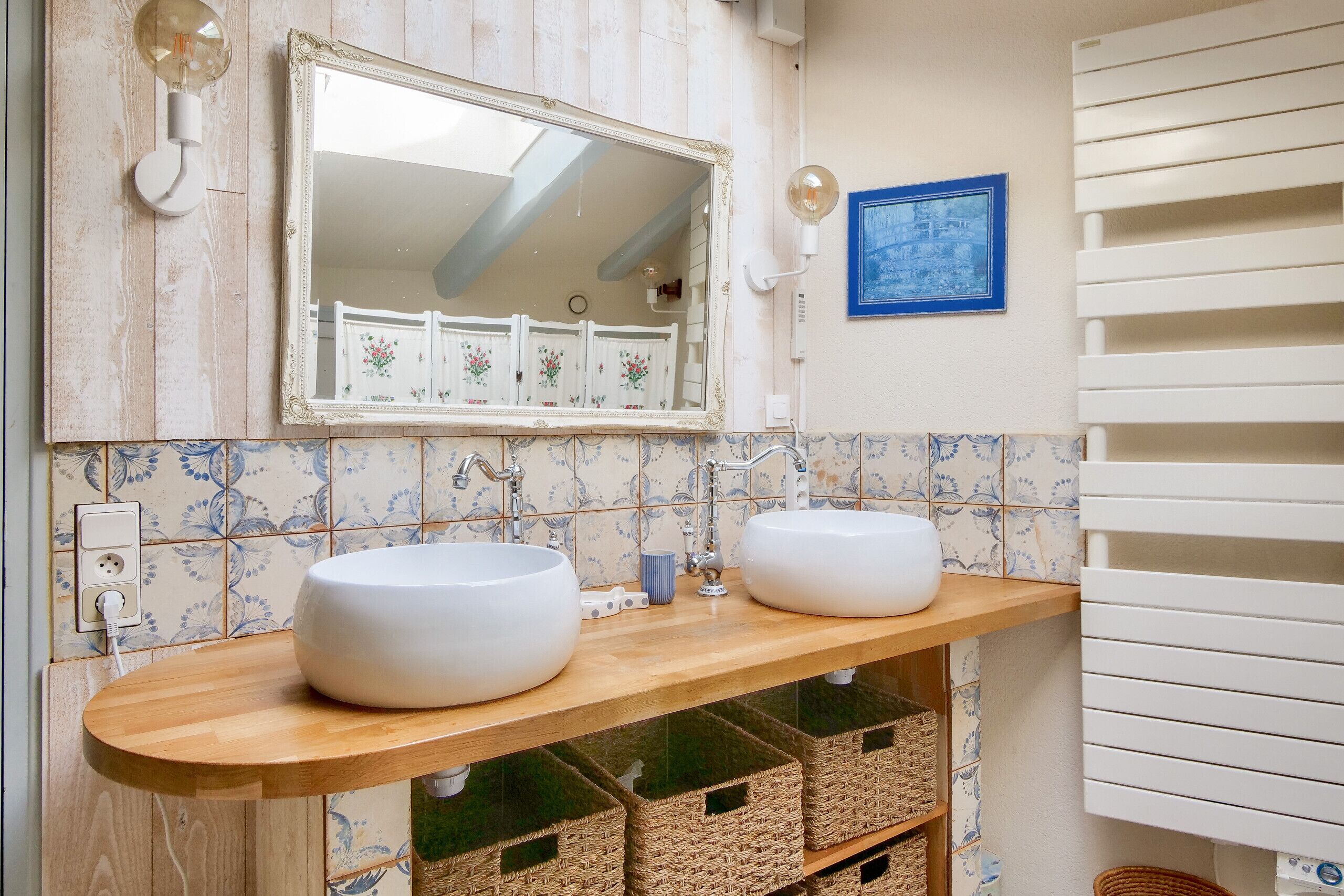 Ein Badezimmer mit zwei weißen Waschbecken, einem Spiegel und einer gefliesten Rückwand.