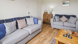 A living room with two grey sofas, a wooden coffee table with wine glasses, a wicker lamp, and a wooden cabinet with a lamp and basket. - Blaenferwig (New Quay)