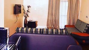 A modern living room with a sofa, a small table with a vase, and a flat-screen TV mounted on the wall. - Limburg Hotel (Port Harcourt)