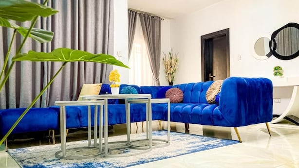 A modern living room with a blue sofa, a glass coffee table, and a large plant. - Limburg Hotel (Port Harcourt)