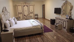 A bedroom with a large bed, a dresser, a TV, and a wardrobe. - Limburg Hotel (Port Harcourt)