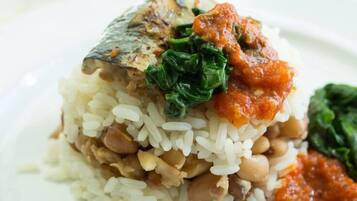 A plate with rice, beans, a piece of fish, and greens.