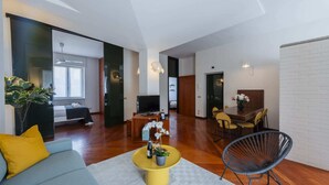 Een moderne woonkamer met een bank, een salontafel en een televisie. Er is een eethoek met een tafel en stoelen.