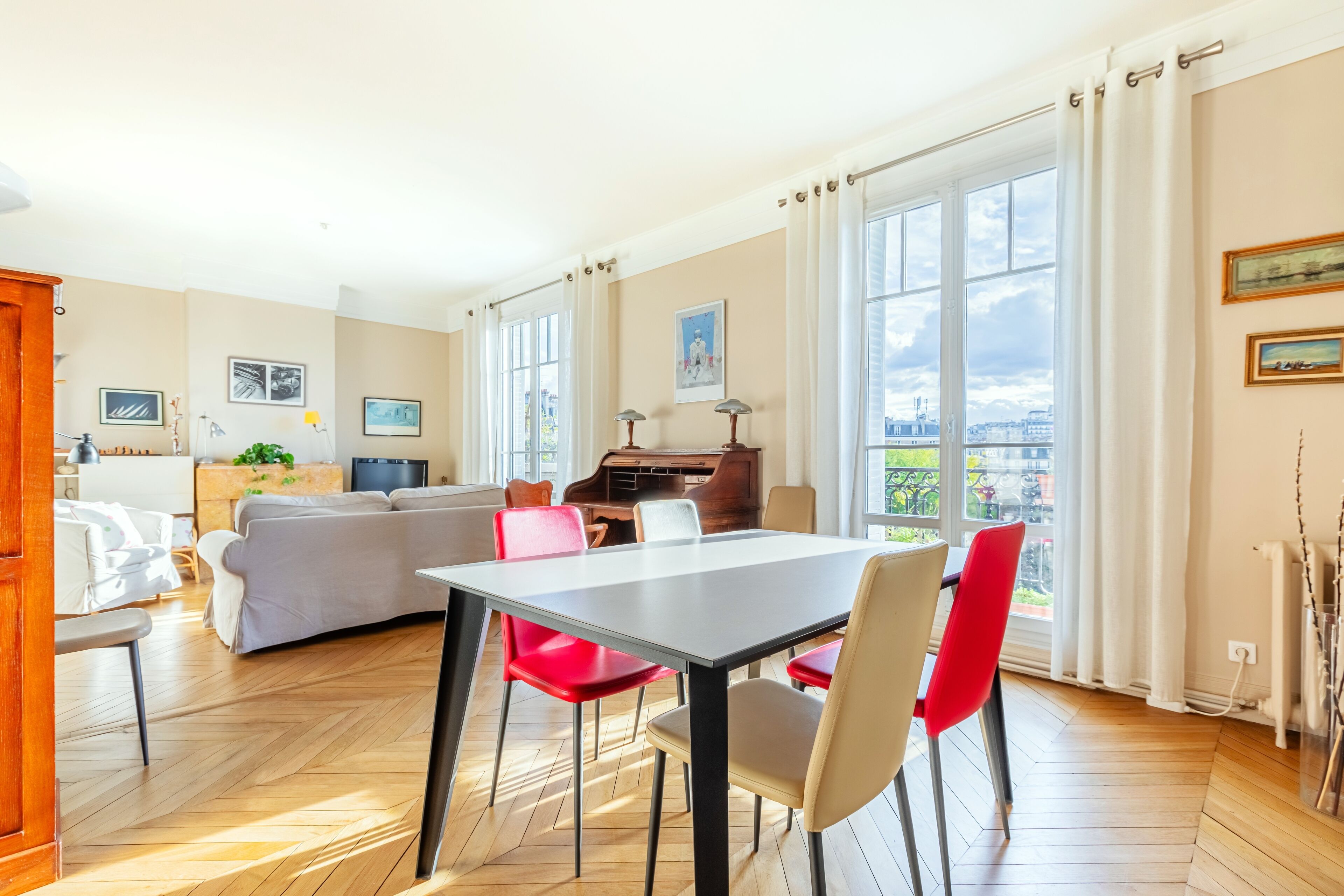 Un salón espacioso con mesa de comedor, sillas rojas y beige, un sofá gris y un piano.