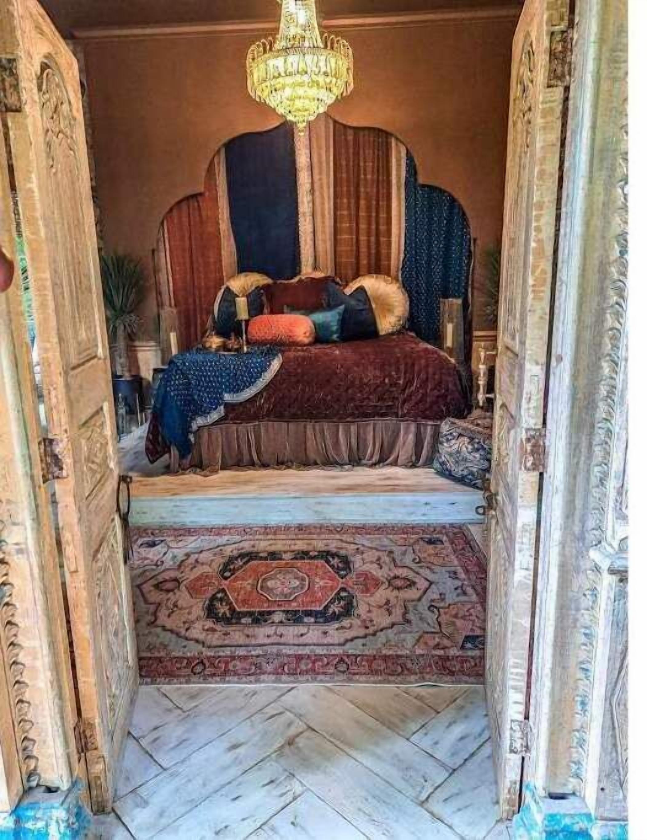 A room with a large bed, ornate curtains, a chandelier, and a patterned rug.