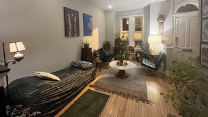 Un salon chaleureux avec un canapé, une table basse et une petite table à manger. Il y a deux tableaux au mur, une lampe et une plante en pot.