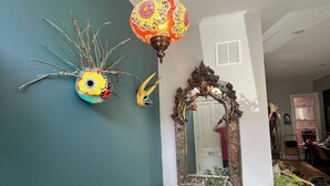 Un couloir avec un mur de couleur turquoise, un miroir décoratif, une lampe suspendue et plusieurs plantes en pot.
