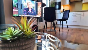 A modern kitchen with white cabinets, a black chair, and a television displaying a news program. - Notting Hill - The One One One! (3) (Greater London)