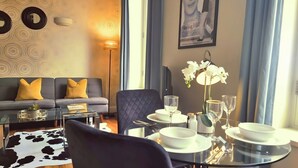 A modern hotel room with a sofa, a dining table set for two, and a large window with curtains. - Notting Hill - The One One One! (3) (Greater London)