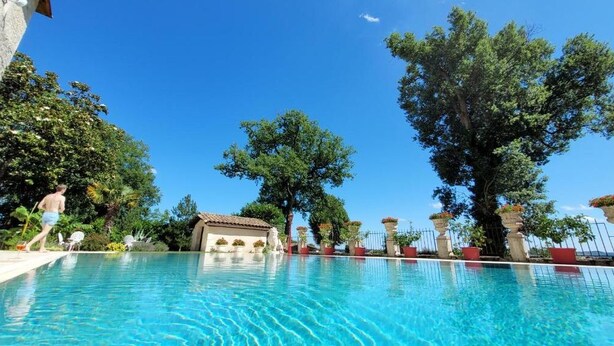 Una piscina con acqua cristallina, circondata da alberi e piante in vaso.