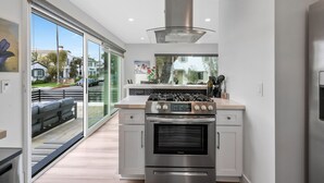 Una cocina moderna con estufa, horno de acero inoxidable y un amplio ventanal con vistas a un barrio residencial.