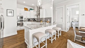 A modern kitchen with white cabinetry, a marble island, and bar stools. - 30A:6-Seater Golf cart, Bikes, Beach Gear, 2 Pools (Inlet Beach)