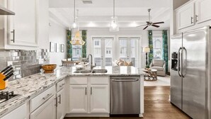 A modern kitchen with white cabinetry, stainless steel appliances, and a central island with a dishwasher. - 30A:6-Seater Golf cart, Bikes, Beach Gear, 2 Pools (Inlet Beach)