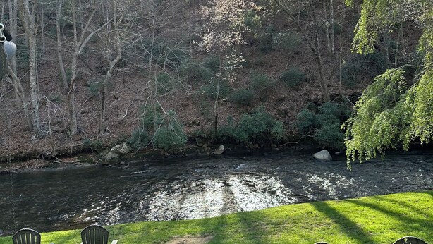 Zona salotto all'aperto lungo il fiume, con sedie e tavolo, circondata da alberi e un prato.