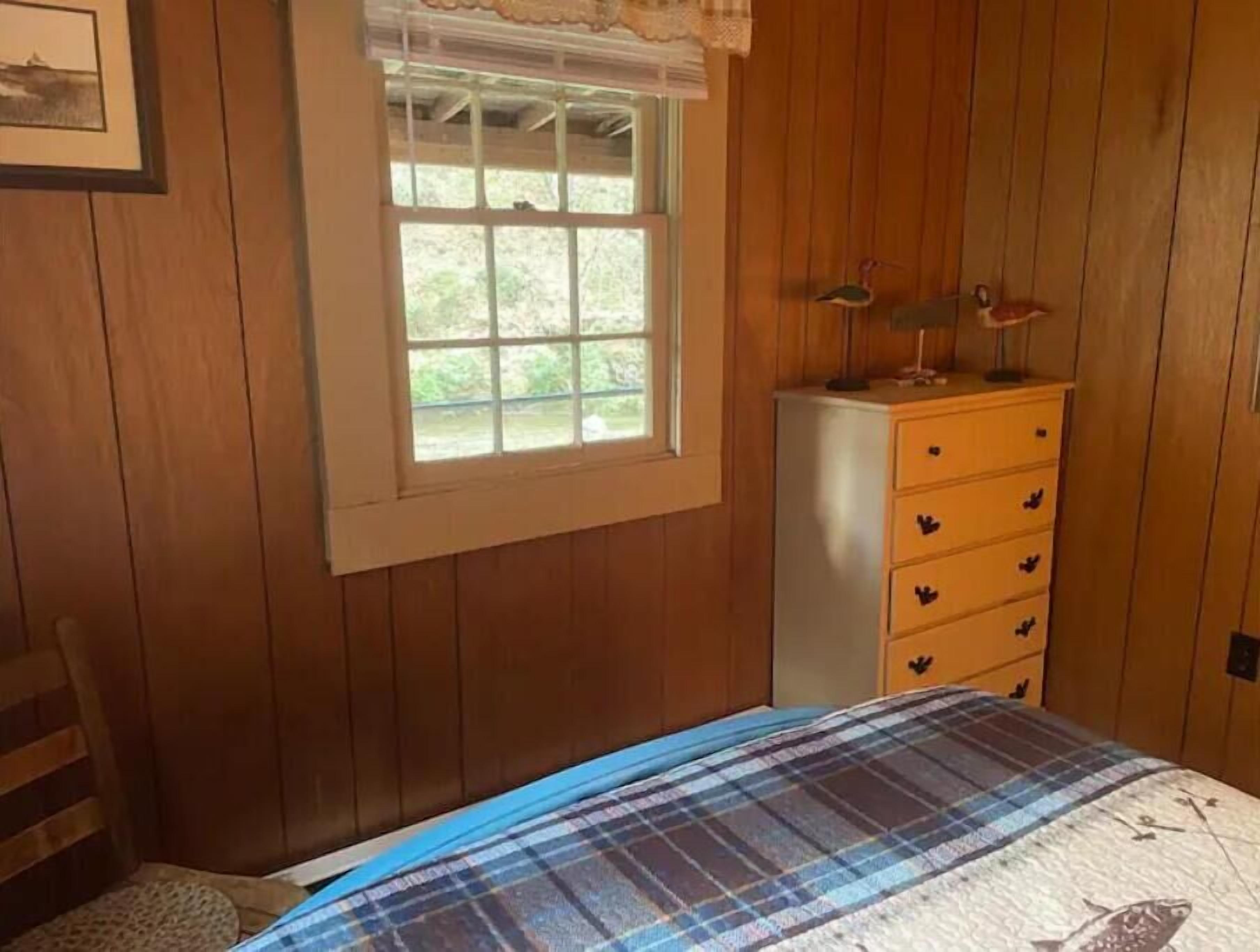 A wooden-paneled room with a bed, a dresser, a window, and a chair.