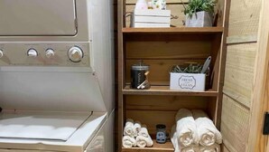 Un angolo lavanderia funzionale con lavatrice, mensole con asciugamani, un cesto e una piccola pianta.