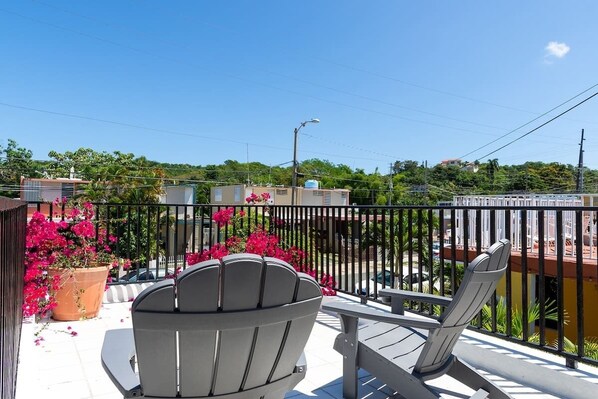 Un balcon avec deux chaises, une balustrade et des plantes en pot ornées de fleurs roses.