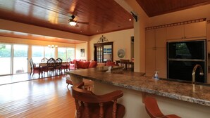 A spacious kitchen with a granite countertop, wooden bar stools, and a large refrigerator. - Discover Melody Lodge, Ontario's Best-Kept Secret Where Tranquil Nature, Adventure, and Comfort Await. (Seeley's Bay)