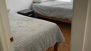 Ein Schlafzimmer mit zwei Betten, einem kleinen Nachttisch und einem Fenster mit durchsichtigen Vorhängen.
