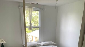 Ein Schlafzimmer mit einem Einzelbett, einem Nachttisch, einem Fenster mit Vorhängen und einem Deckenventilator.