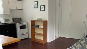 Ein kleines Zimmer mit einem Bett, einer Küchenzeile und einem Holzbücherregal.