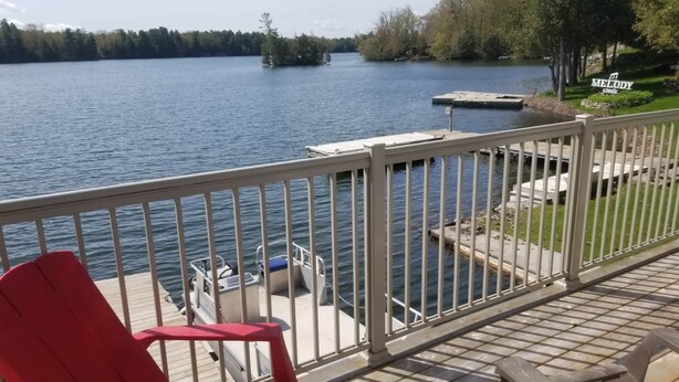 Una terraza con una silla roja, una mesa de madera y vistas a un lago con un muelle y un bote.