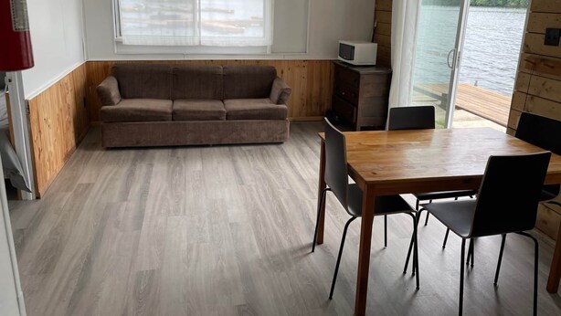 En hyggelig hytte med sofa, spisebord, stole og udsigt til en sø.