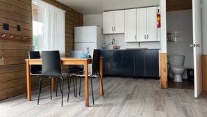 Et lille køkken med hvide skabe, en sort bordplade og et træspisebord med fire stole.