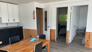 Et moderne værelse med et træspisebord, sorte stole, et tekøkken med hvide skabe og en synlig brandslukker.