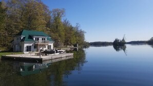 A lakeside house with a green roof, a dock, and a calm lake. - Discover Melody Lodge, Ontario's Best-Kept Secret Where Tranquil Nature, Adventure, and Comfort Await. (Seeley's Bay)