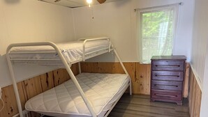 A bunk bed with a wooden headboard, a dresser with multiple drawers, and a window with a view of trees. - Discover Melody Lodge, Ontario's Best-Kept Secret Where Tranquil Nature, Adventure, and Comfort Await. (Seeley's Bay)