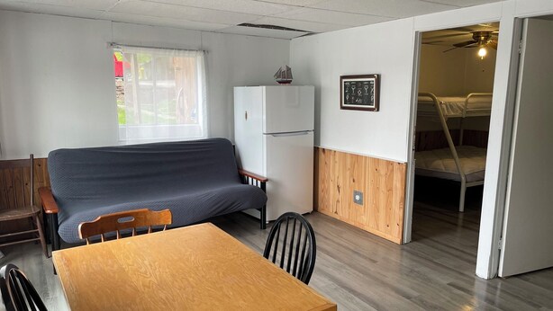 A compact living space with a sofa, a dining table, a refrigerator, and a bunk bed. - Discover Melody Lodge, Ontario's Best-Kept Secret Where Tranquil Nature, Adventure, and Comfort Await. (Seeley's Bay)