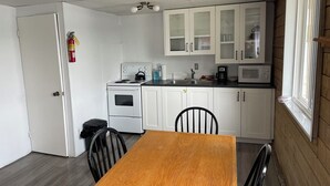 A compact kitchen with white cabinets, a stove, a microwave, and a dining table with chairs. - Discover Melody Lodge, Ontario's Best-Kept Secret Where Tranquil Nature, Adventure, and Comfort Await. (Seeley's Bay)
