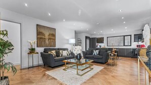Ein modernes Wohnzimmer mit zwei Sofas, einem Glastisch und einem Essbereich mit einem weißen Stuhl.