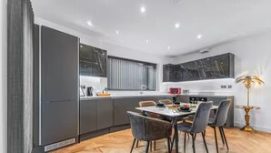Eine moderne Küche mit dunklen Schränken, einer Marmor-Spritzschutzwand und einem Essbereich mit rundem Tisch und Stühlen.