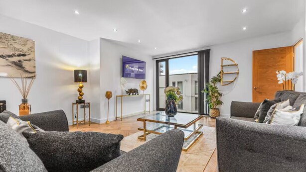Ein modernes Wohnzimmer mit grauen Sofas, einem Glastisch und einem großen Fenster.