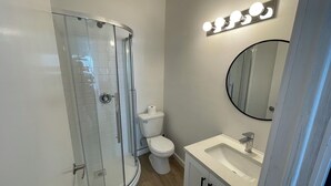 Et badeværelse med en glasvæg omkring brusebadet, toilet og et spejl over vasken.