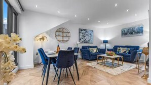 Ein modernes Wohnzimmer mit Essbereich, blauen Sofas und einem Fischgrätparkett.