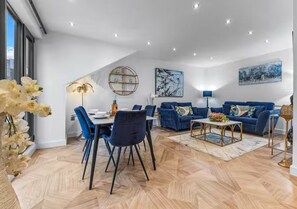 A modern living room with a dining area, blue sofas, and a herringbone floor pattern.