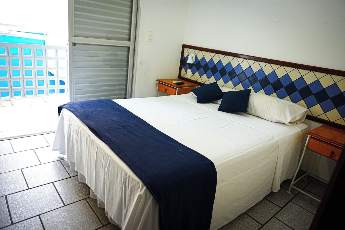 A hotel room with a large bed, a nightstand, a bedside table, and a view of the outside through a sliding door.