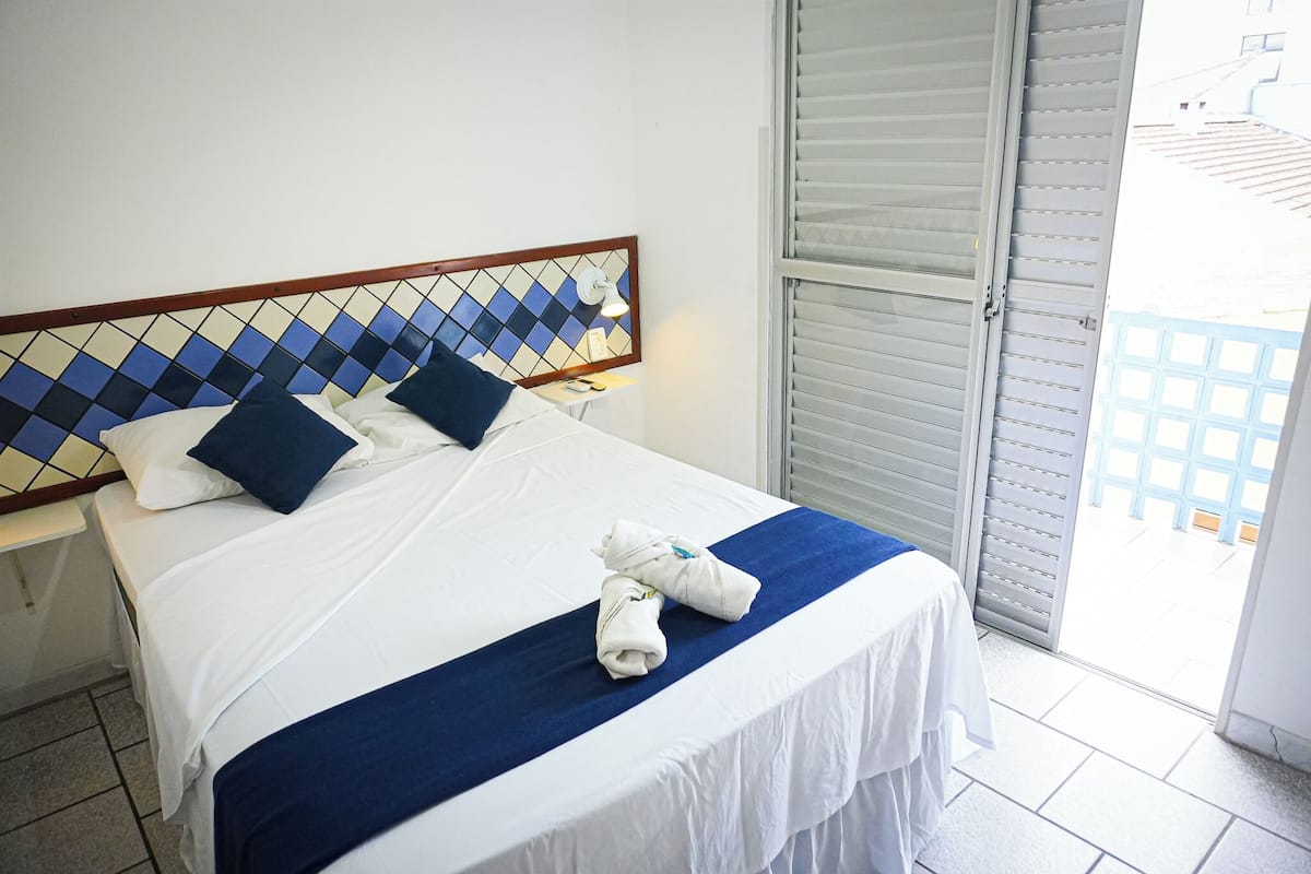 A hotel room with a bed, a nightstand, a wall-mounted lamp, and a view through a door.